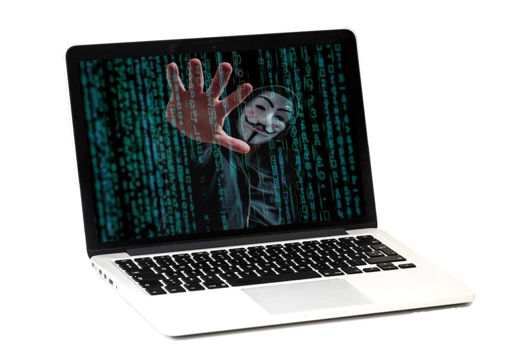 A computer with code on the screen with an "Anonymous" hacker superimposed.